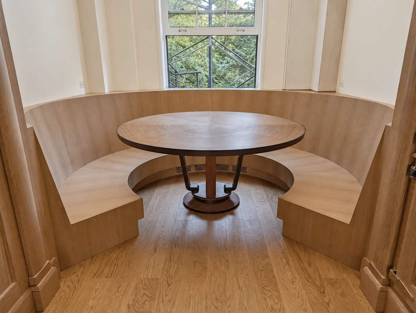 Completed curved wood banquette fitted around an angled window niche with a round radial-grain pedestal table