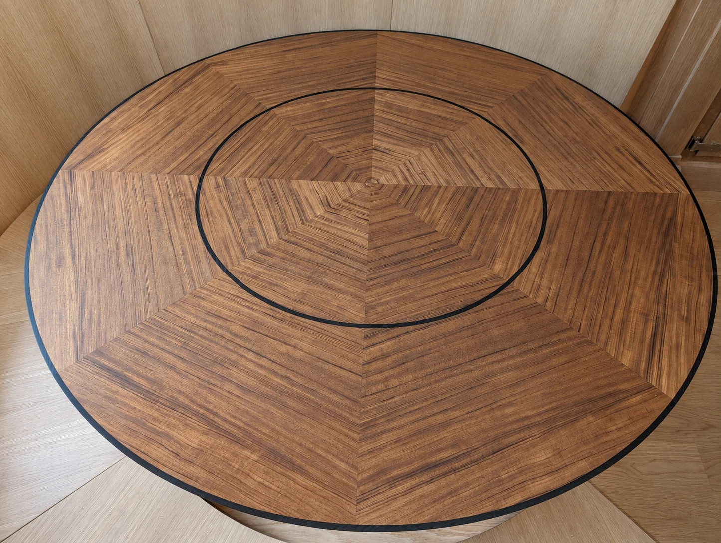 Close view of the curved banquette table with radial wood veneer segments and a dark circular inset ring