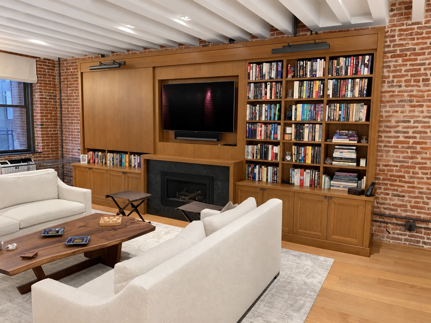 Completed oak bookcase and media wall in Lower Manhattan, with sliding wood panels, bookshelves and paneled storage around a television and fireplace