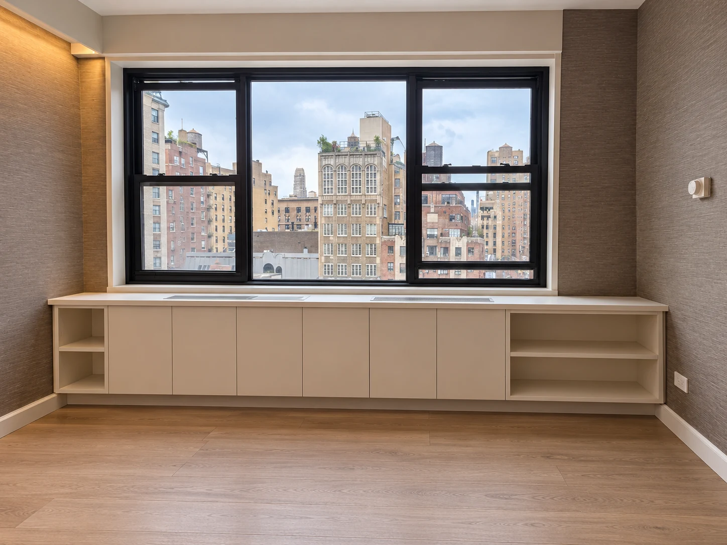 Lenox Hill fitted storage beneath a black-framed window, with pale flush cabinet fronts, open shelves at both ends and inset countertop ventilation grilles
