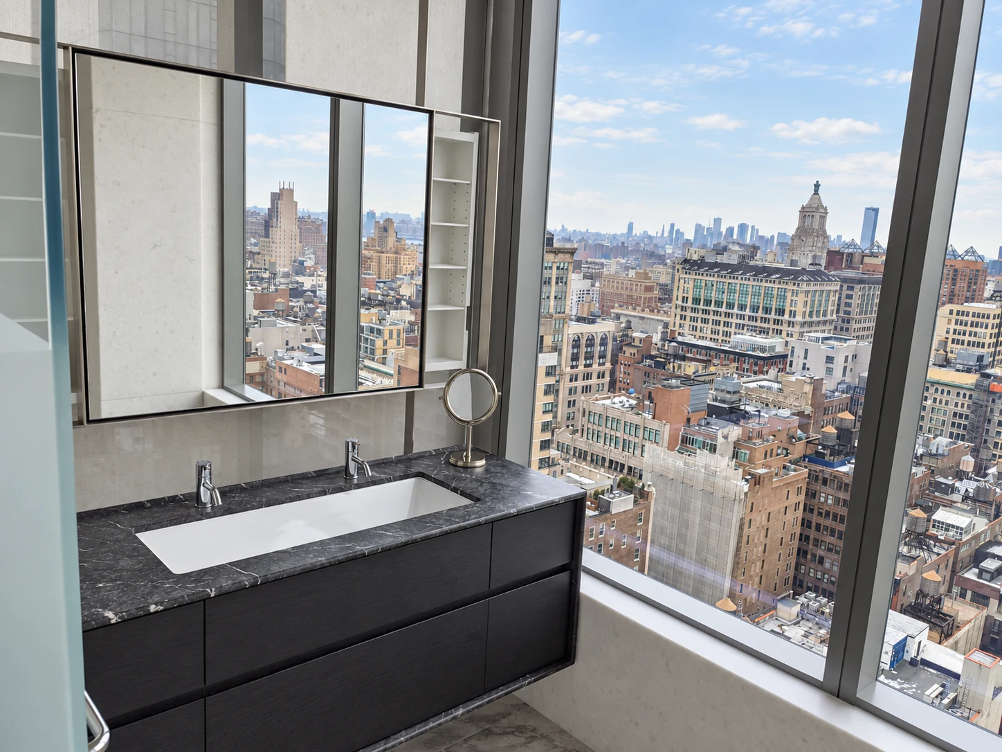 Dark floating bathroom vanity in the Flatiron District with a stone countertop, inset basin and mirrored storage beside panoramic city windows